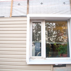 Wall covering of the frame house with panels of vinyl siding of gray color. Decorating the house with siding. The master updates the look of the old house with siding.