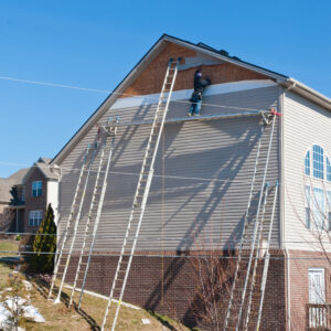 Workers installing plastic siding panels on two story house.